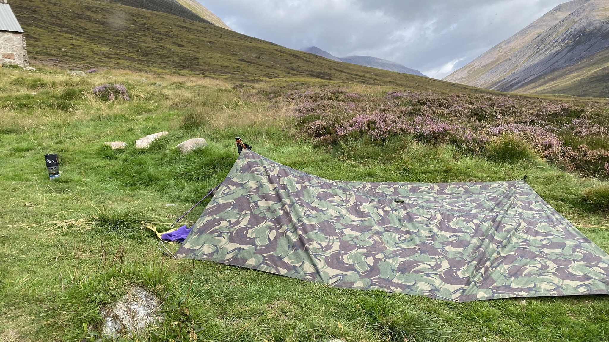 A tarp shelter pitched on grass outside Corrour Bothy