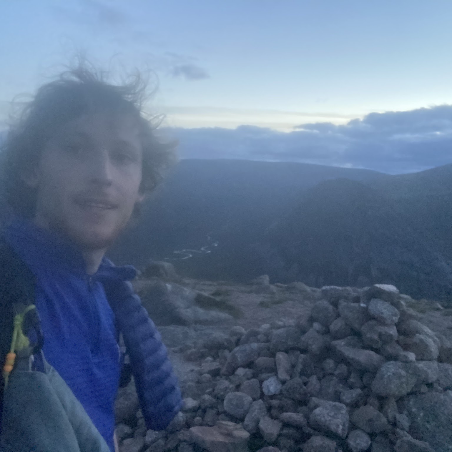 Summit selfie at dusk beside a cairn
